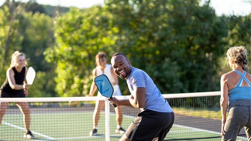 A group of people playing pickleball on a court with paddles, enjoying a friendly match in the open air