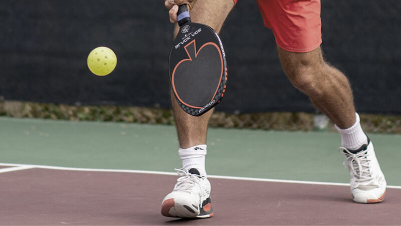 A person playing pickleball with paddle and ball on a court, wearing pickleball shoes.