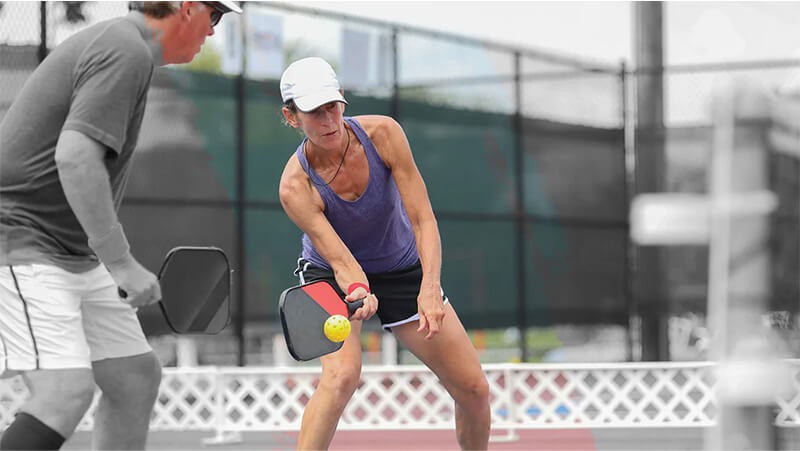 A man and woman playing pickleball on a court, both wearing sportswear and holding Pickleball paddles.